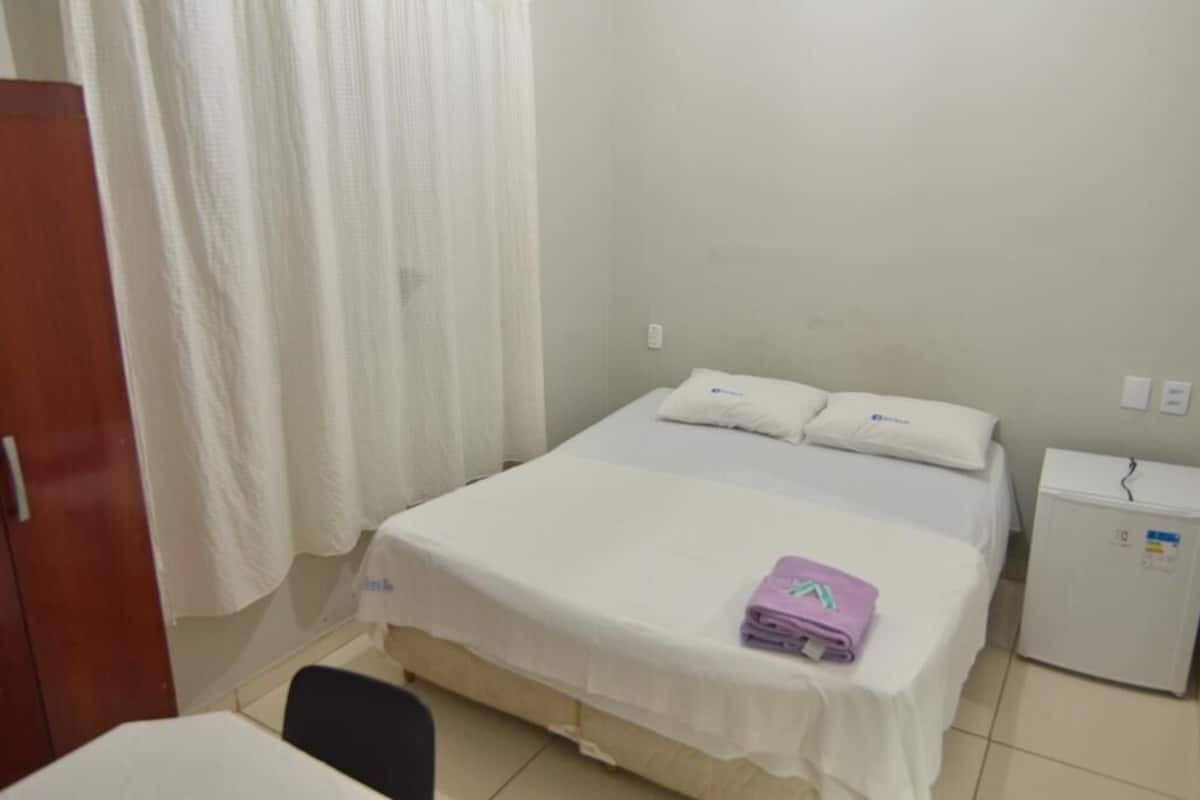 A small, clean room with a single bed, a small table, and a refrigerator.