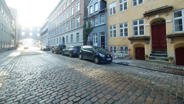 Een straat met keien, geflankeerd door historische gebouwen, geparkeerde auto's en een fiets.