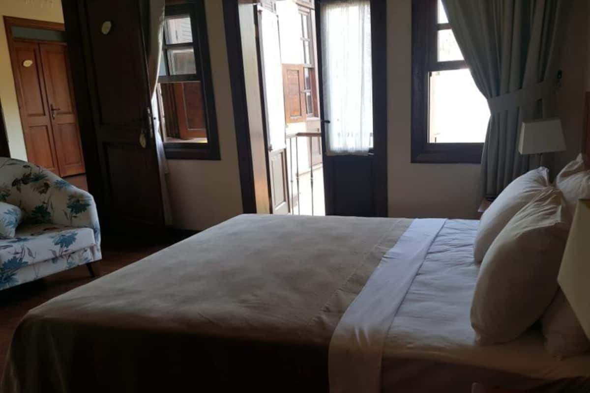 Quarto de hotel com uma cama, uma cadeira, mesa de cabeceira e uma janela.