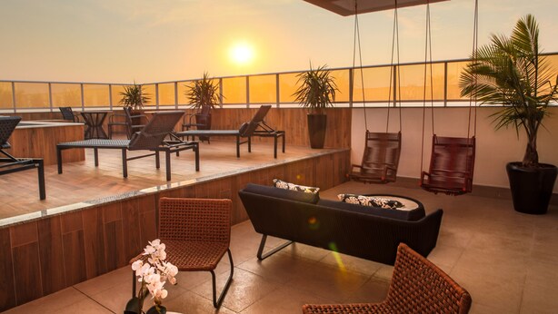 Una terraza en la azotea con mobiliario de mimbre, plantas en macetas y vistas a la puesta de sol.