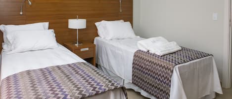 A hotel room with two single beds, a wooden headboard, a nightstand with a lamp, and a bathroom door.