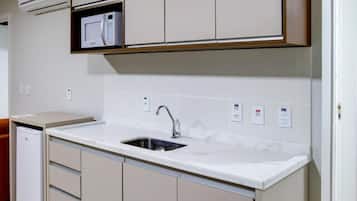 A compact kitchen with white cabinetry, a built-in microwave, and a stainless steel sink.