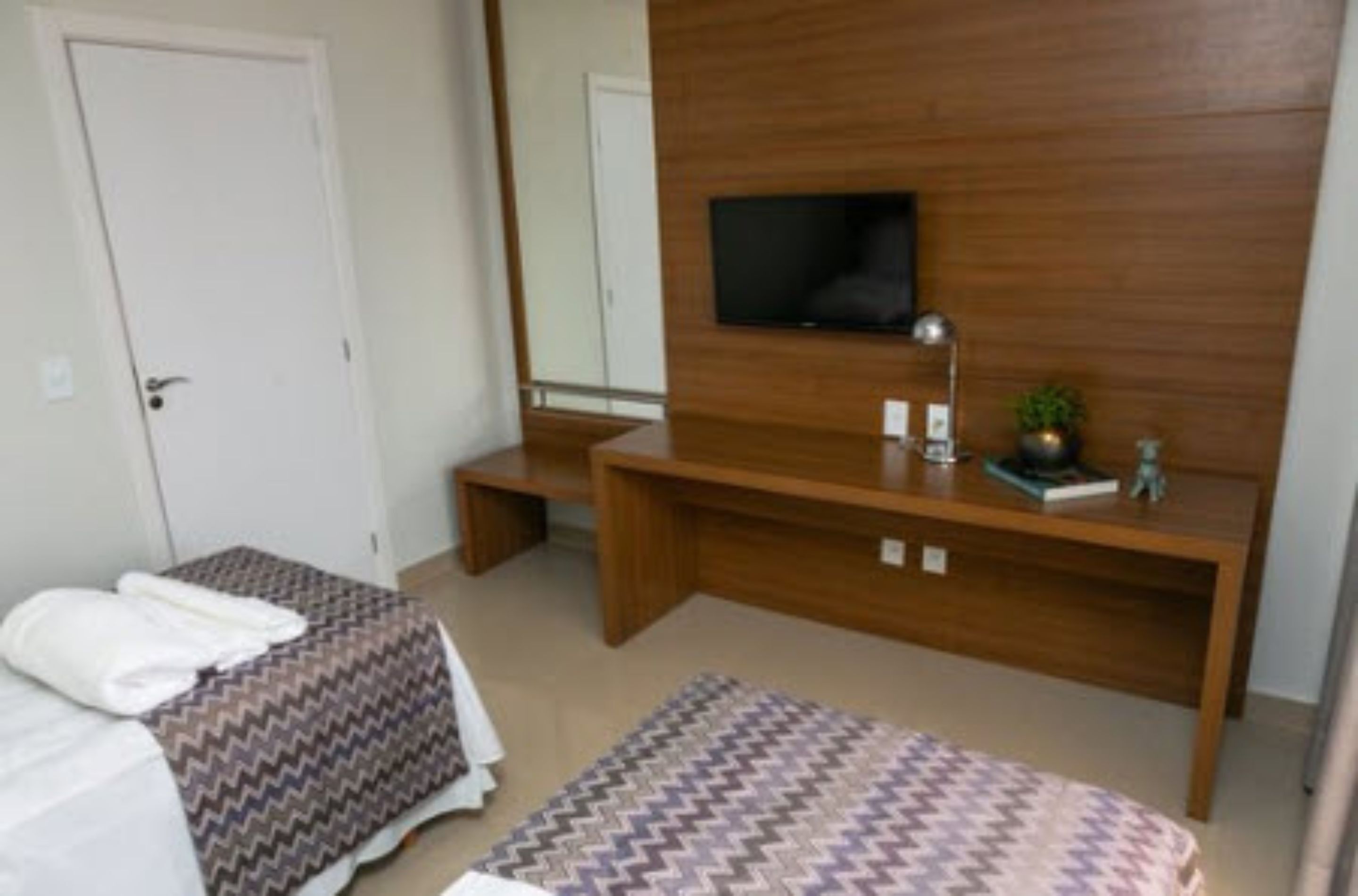 Una habitación de hotel con una cama, una mesita de noche, un televisor montado en la pared y un espejo.