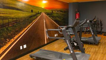 A gym with treadmills, stationary bikes, and a wall mural of a road leading to a sunset.