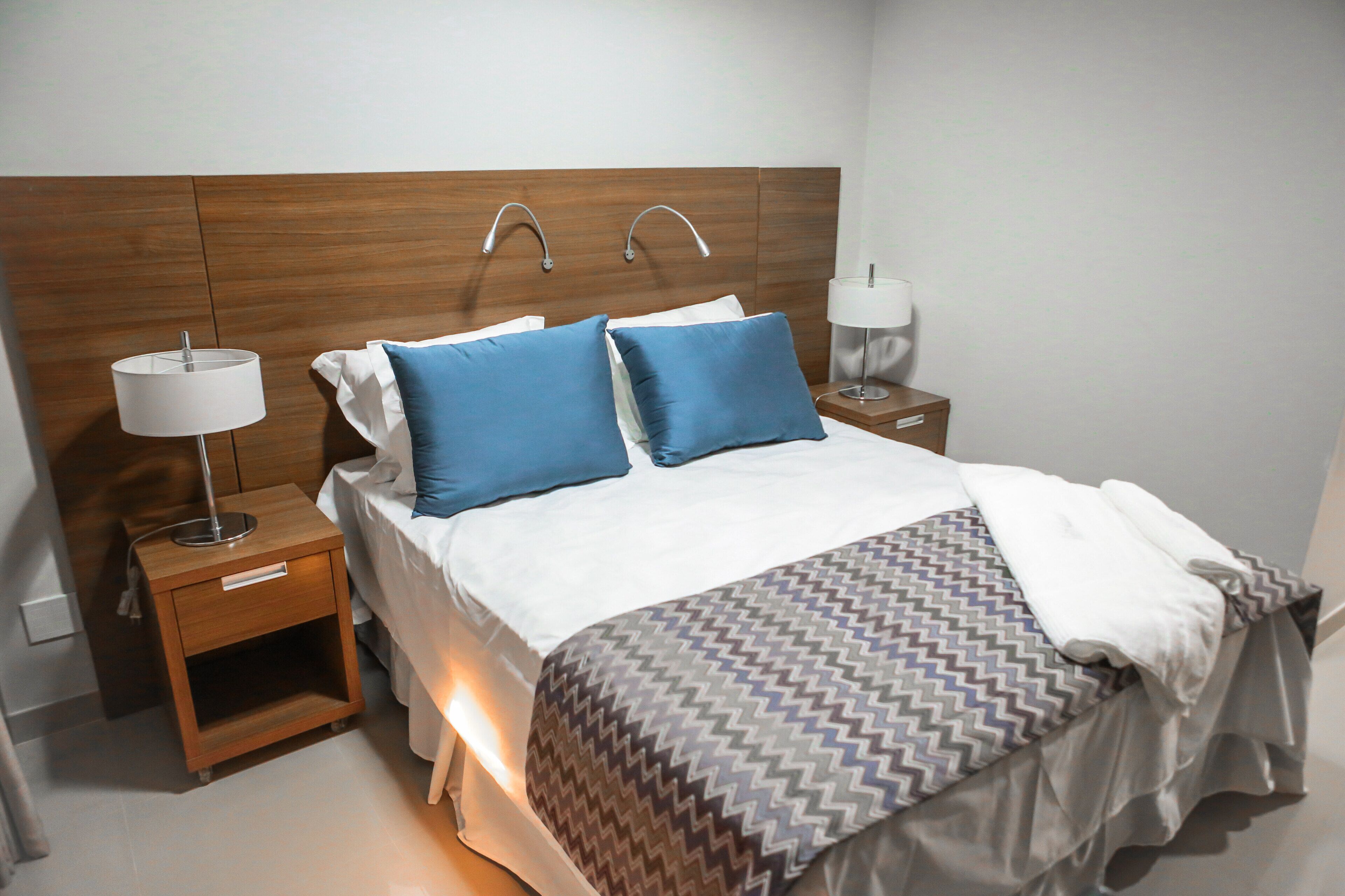 Un lit bien fait, avec une couvre-lit à motifs, deux oreillers et une lampe de chevet posée sur une table de nuit en bois.