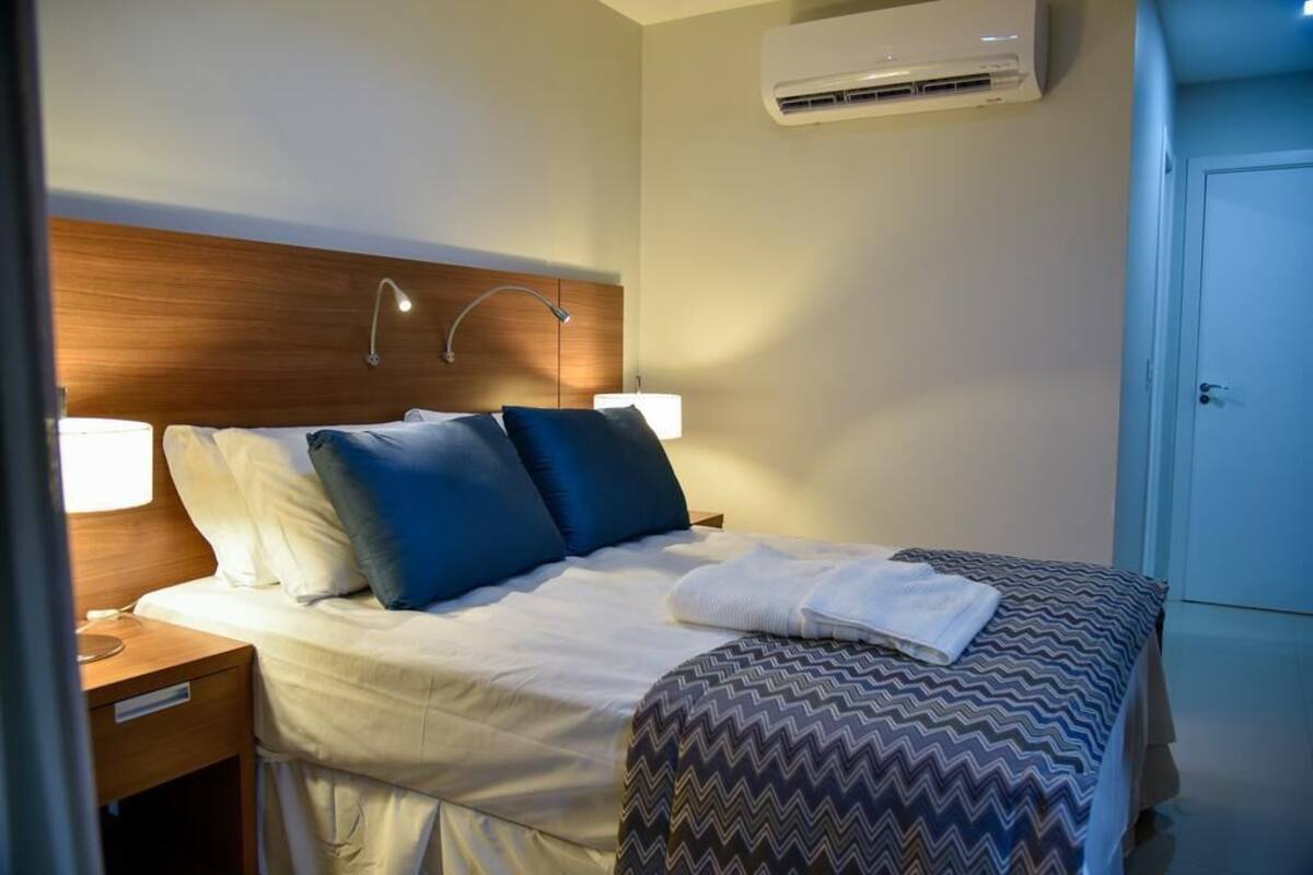Una habitación de hotel con cama, lámparas de noche, unidad de aire acondicionado y una puerta.