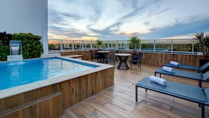 Un área de piscina en la azotea con terraza de madera, sillas de descanso y una mesa con sillas.