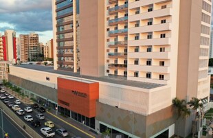 Un hotel de varios pisos con una fachada anaranjada llamativa, varios balcones y un estacionamiento al frente.