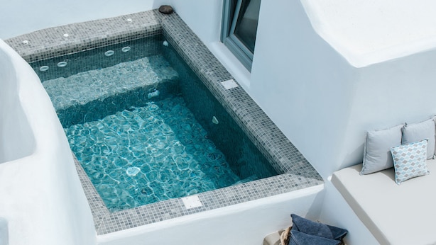 A modern, minimalist bathroom with a built-in bathtub, a small window, and a wicker basket with towels. - Il Melograno Traditional Cave House (Santorini)