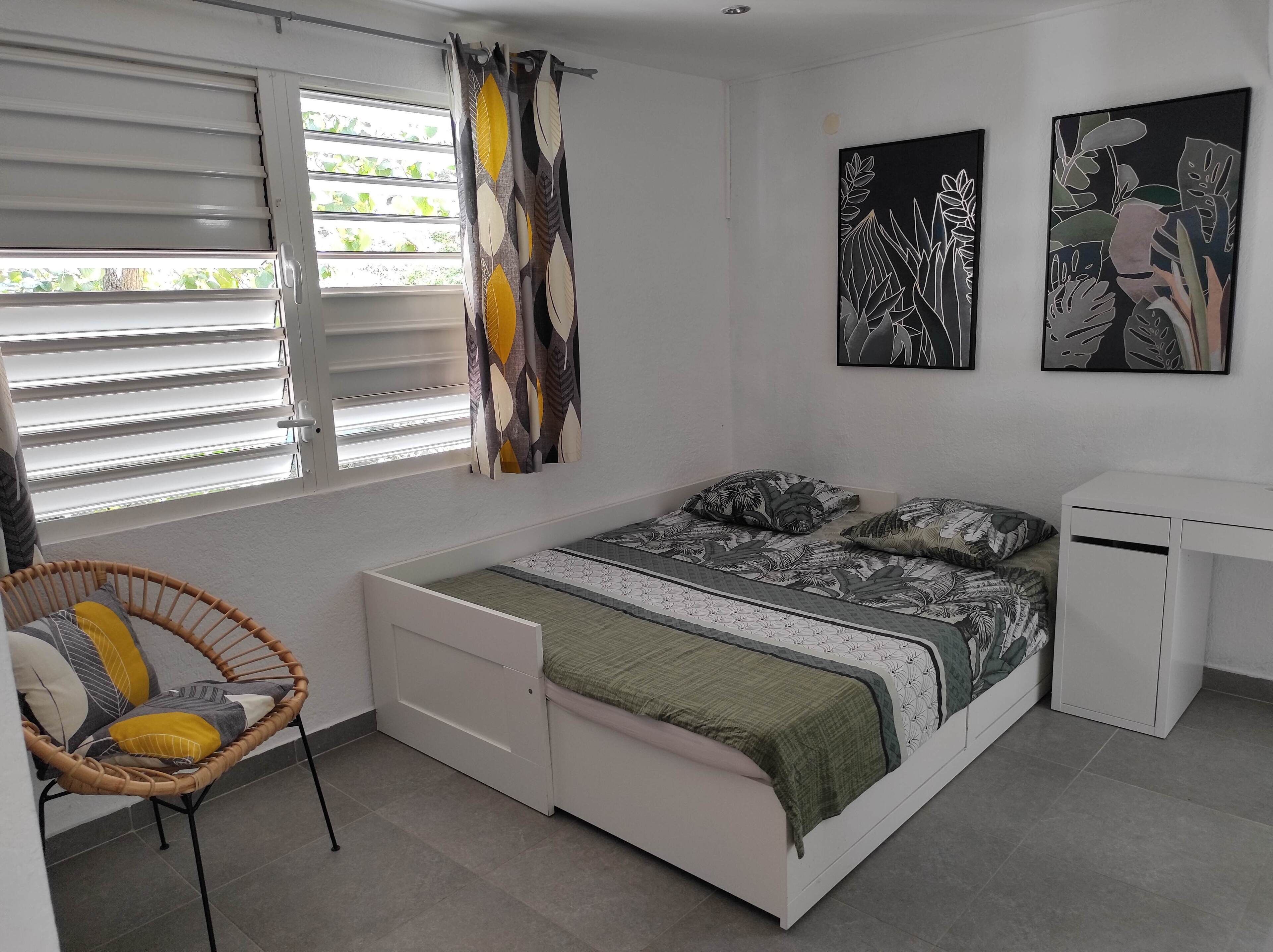 A bedroom with a bed, a chair, a desk, and two wall-mounted paintings.