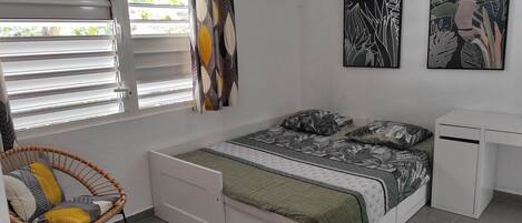 A bedroom with a bed, a chair, a desk, and two wall-mounted paintings.