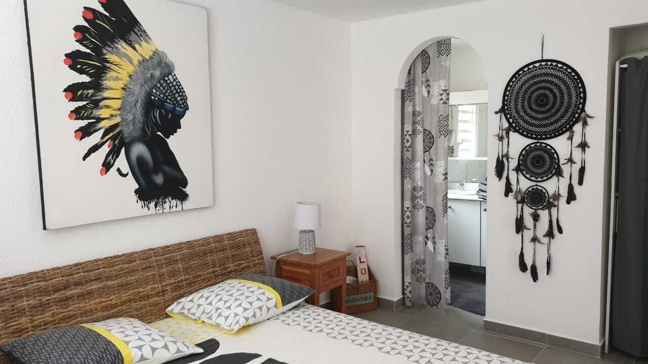 A bedroom with a bed, pillows, a nightstand, a wall art piece, and a dreamcatcher.