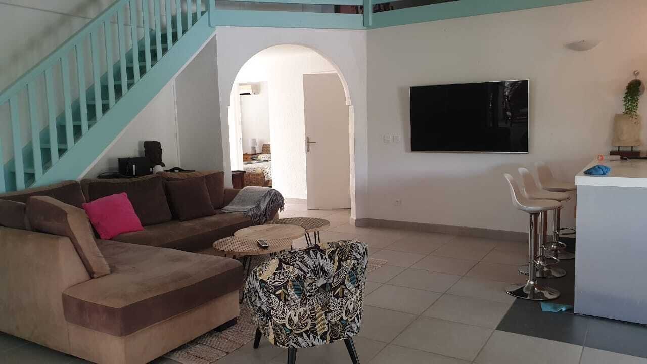A spacious living area with a sofa, a patterned armchair, a small round table, and a TV mounted on the wall.