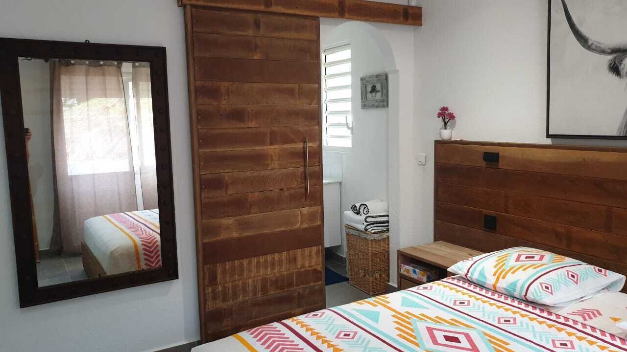 A bedroom with a wooden headboard, a bed with patterned bedding, a mirror, and a small wicker basket.