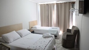 Habitación de hotel con dos camas, una silla, un televisor y cortinas.