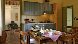 A cozy kitchen with wooden cabinets, a dining table set with plates, cups, and a vase of flowers. - Poggio Montali (Monte Roberto)