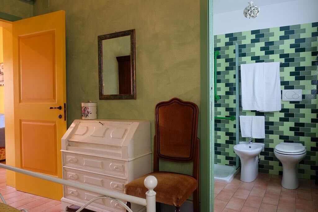 Une salle de bain avec une porte jaune, une commode blanche, une chaise marron, un miroir, un lavabo et des toilettes.