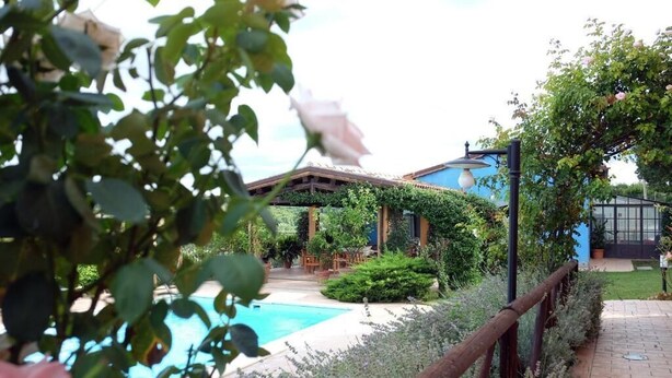 A pool area with a wooden fence, a covered seating area, and a building with a blue roof. - Poggio Montali (Monte Roberto)