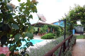 A pool area with a wooden fence, a covered seating area, and a building with a blue roof. - Poggio Montali (Monte Roberto)