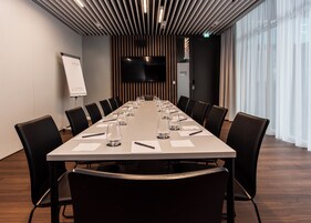 Un salón de conferencias con una larga mesa, sillas negras, una pizarra y una pantalla de televisión.