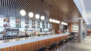 Una zona de bar moderna con pared de listones de madera, taburetes y una máquina de café.