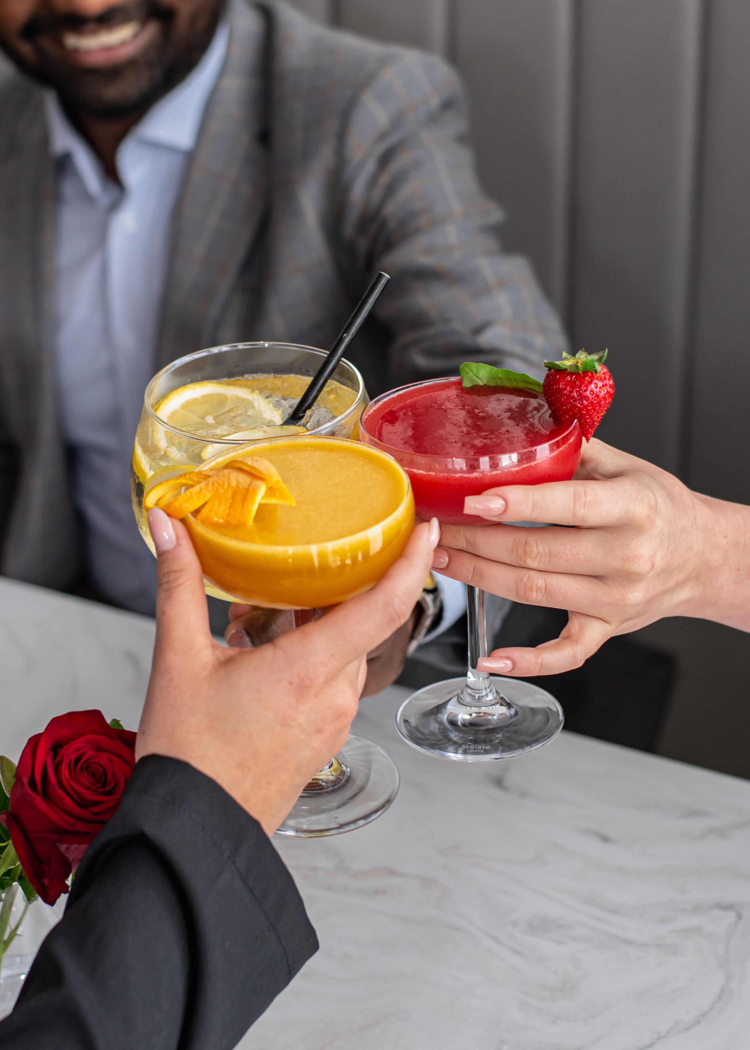 A person holding a yellow drink with a straw and a red drink garnished with a strawberry and a leaf.