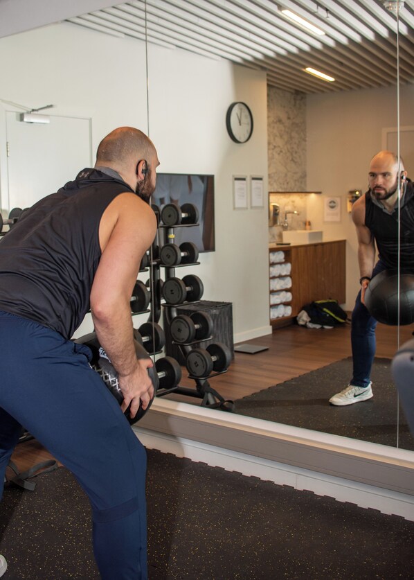 A gym with a mirrored wall, weight racks, and a clock on the wall.