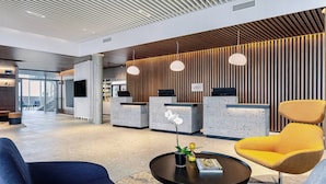 Un área de recepción moderna con un panel de pared de madera, un mostrador de recepción y asientos con una silla azul y amarilla.