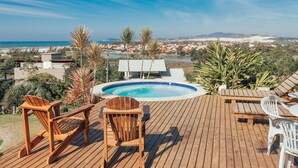 Une terrasse en bois avec une piscine, des chaises et une vue sur la plage et la ville.
