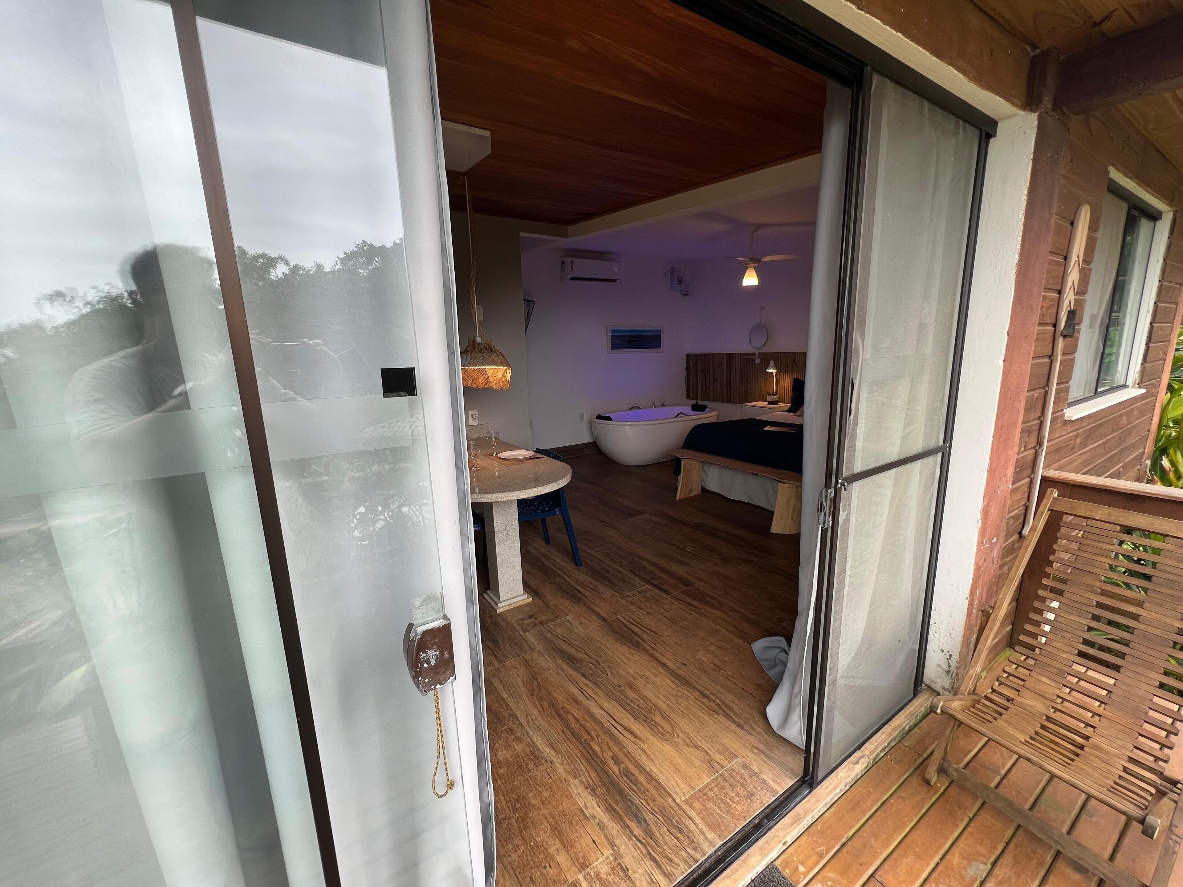 Una habitación con piso de madera, una bañera, una cama y una pequeña mesa con una silla.