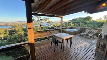 Una terraza de madera con un jacuzzi, sillas de descanso y una mesa con sillas.