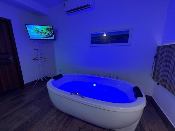 A modern bathroom with a freestanding bathtub, a mounted TV, and a small window. - Chalés & Bangalôs Ibiraquera (Imbituba)