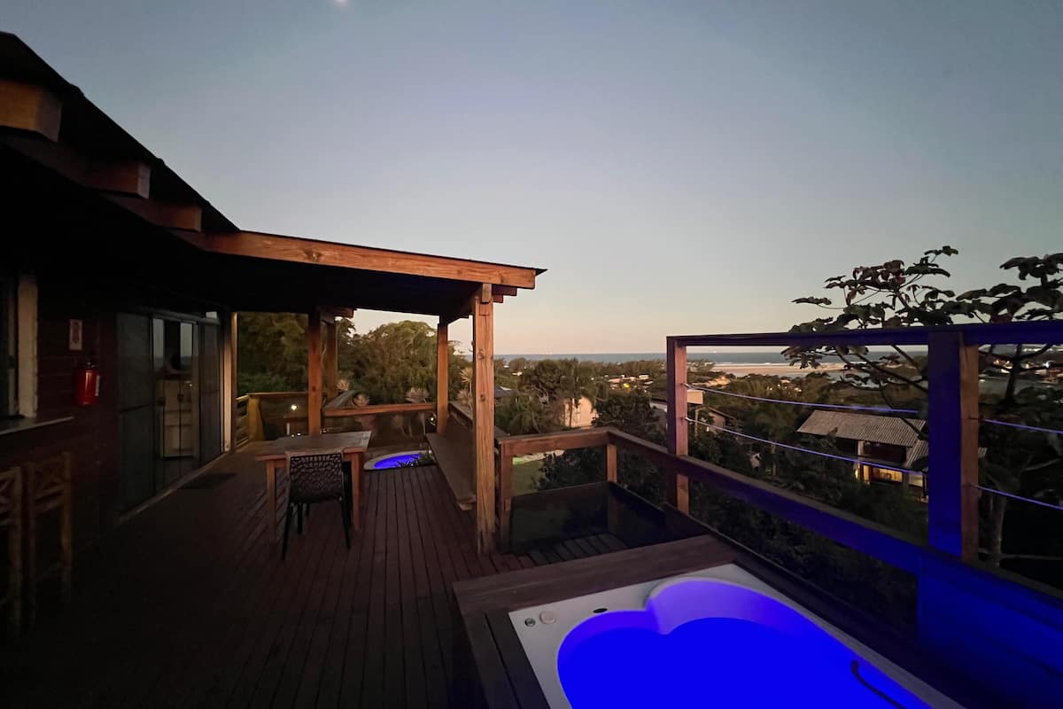 A wooden deck with a hot tub and seating area, overlooking a scenic landscape.