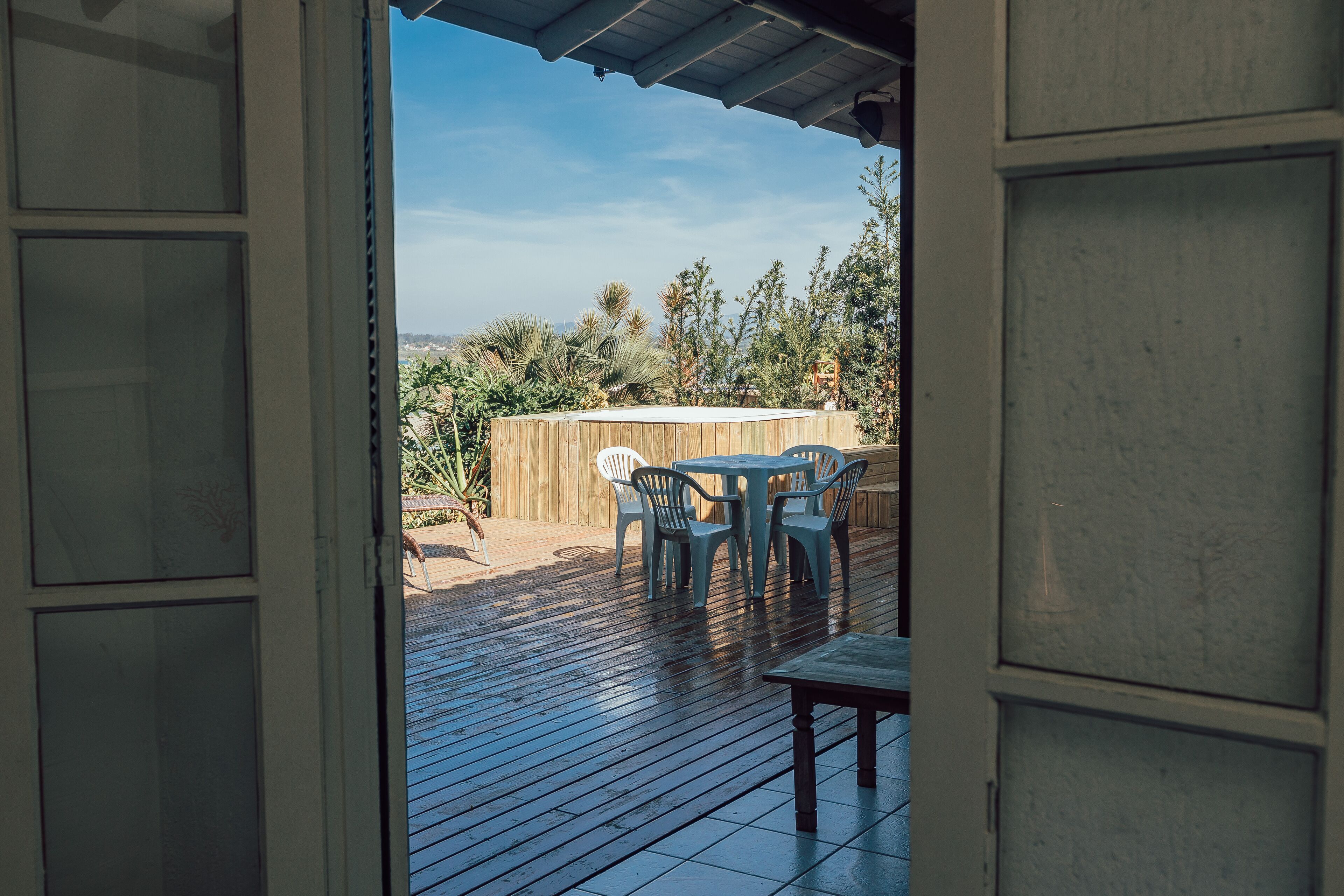 Una puerta abierta que da a un patio exterior con terraza de madera, una mesa y sillas.