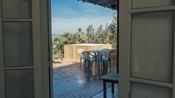 Una puerta abierta que da a un patio exterior con terraza de madera, una mesa y sillas.