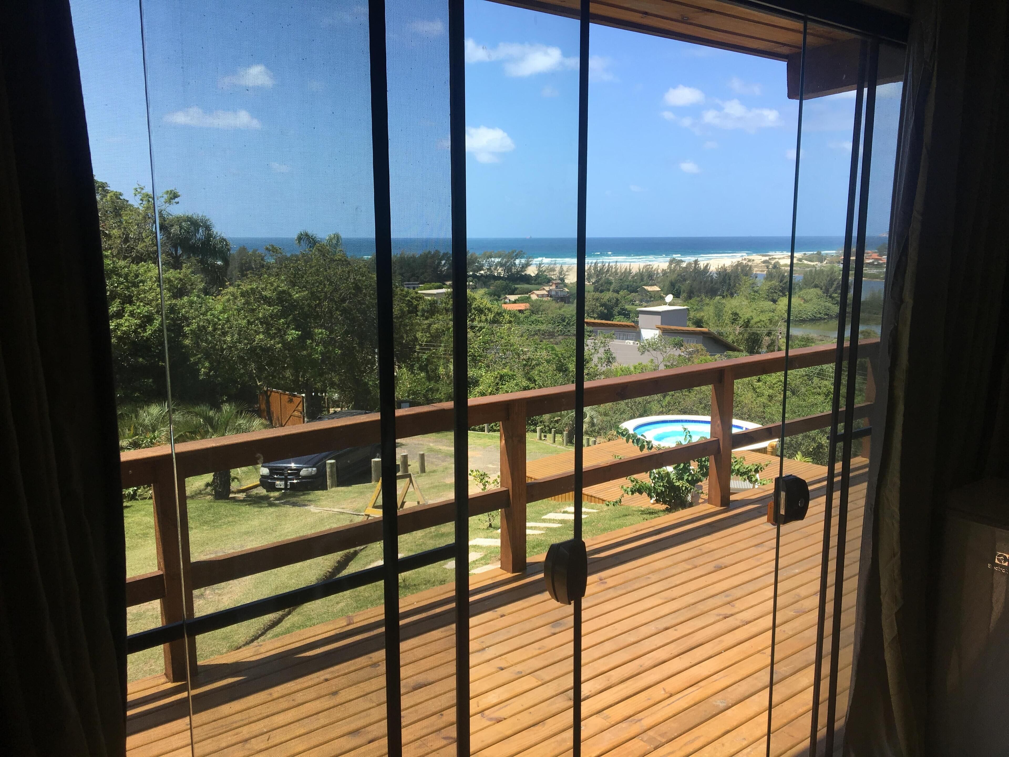 A balcony with a view of a swimming pool, lush greenery, and a distant ocean.