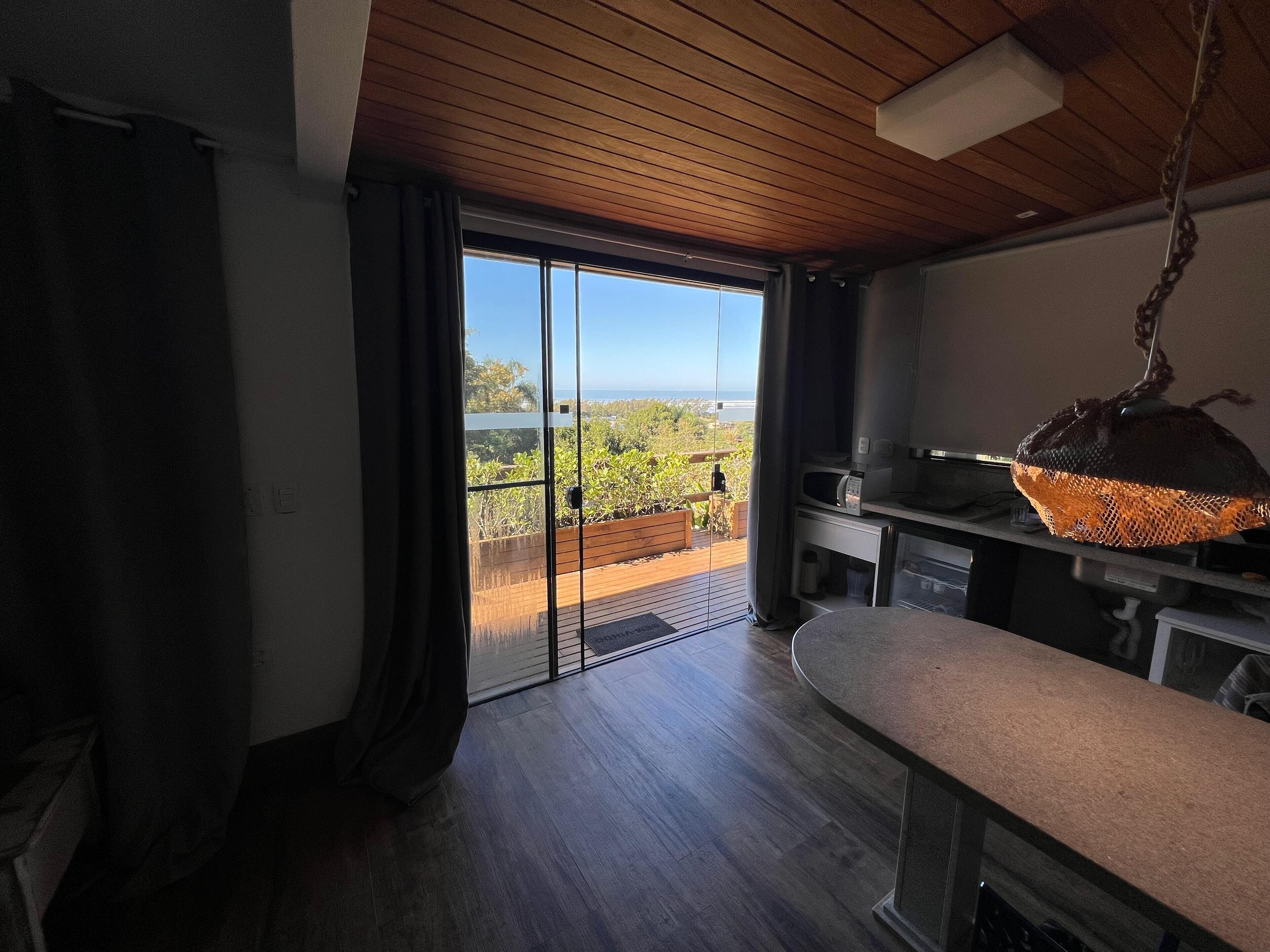 A modern kitchen with a wooden ceiling, a large sliding glass door leading to a balcony, and a hanging light fixture.