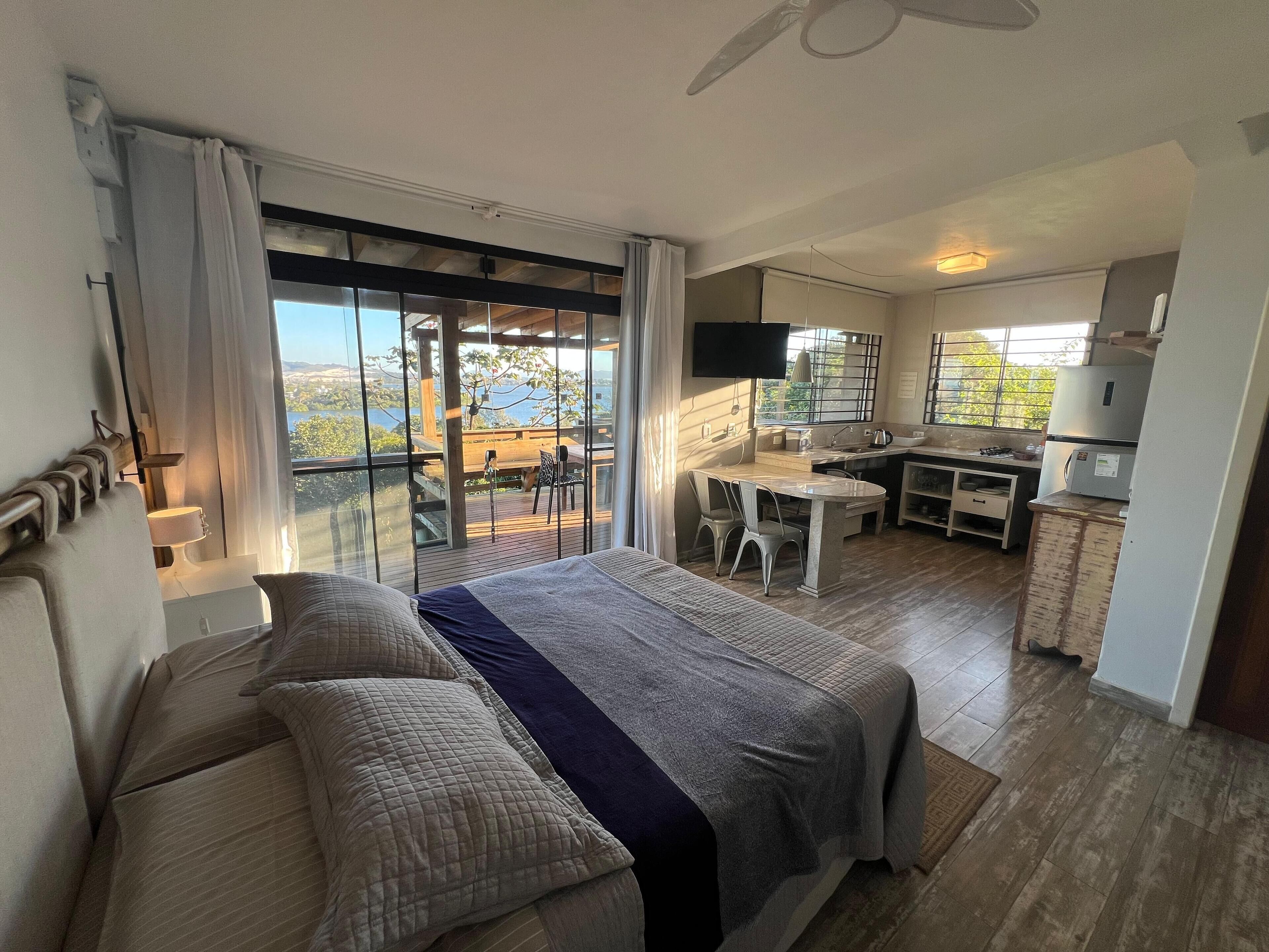 Une chambre avec un grand lit, un balcon avec une table et des chaises, et un coin cuisine.