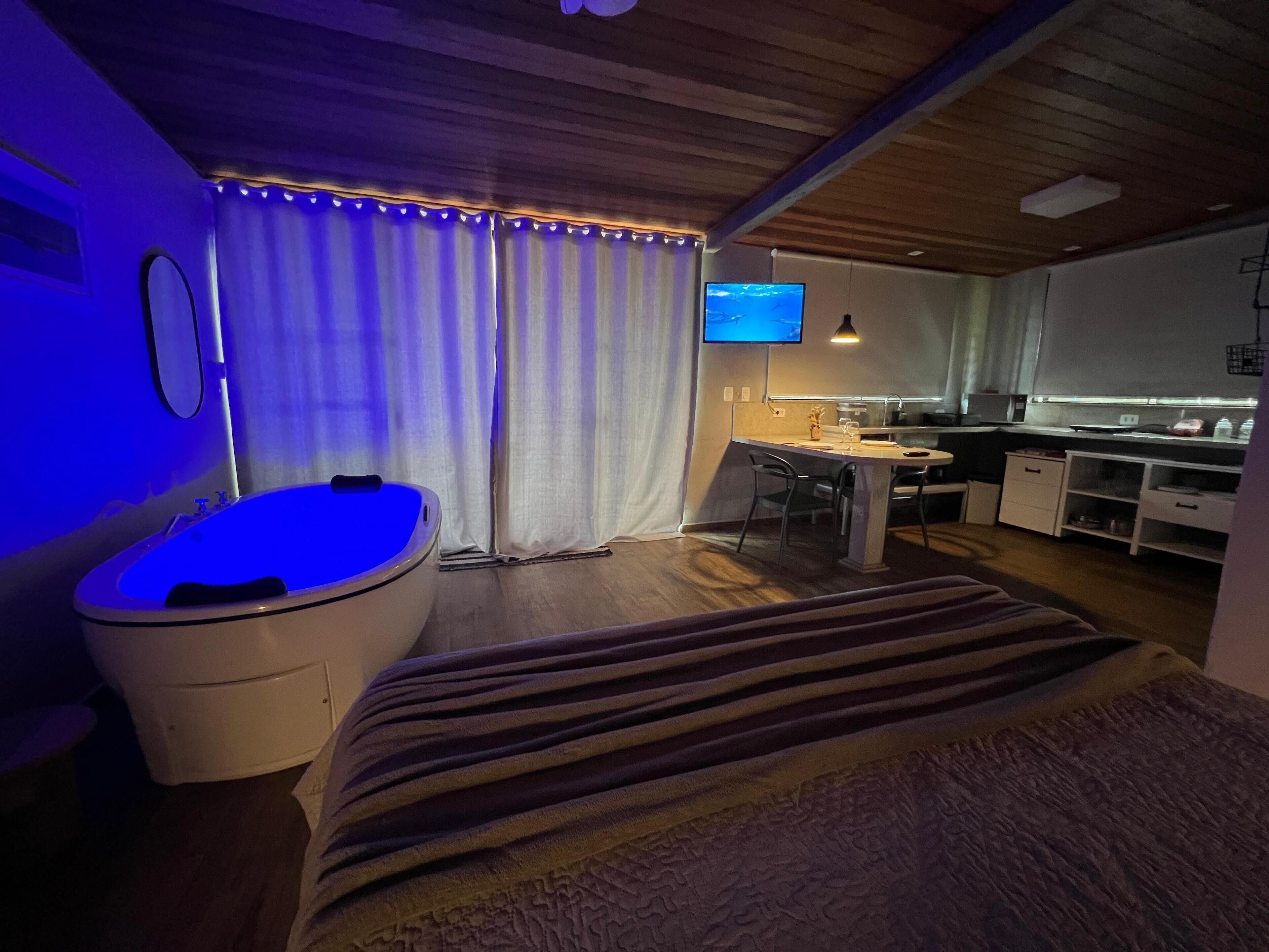 Un dormitorio moderno con una cama grande, una bañera integrada, un escritorio y un televisor.