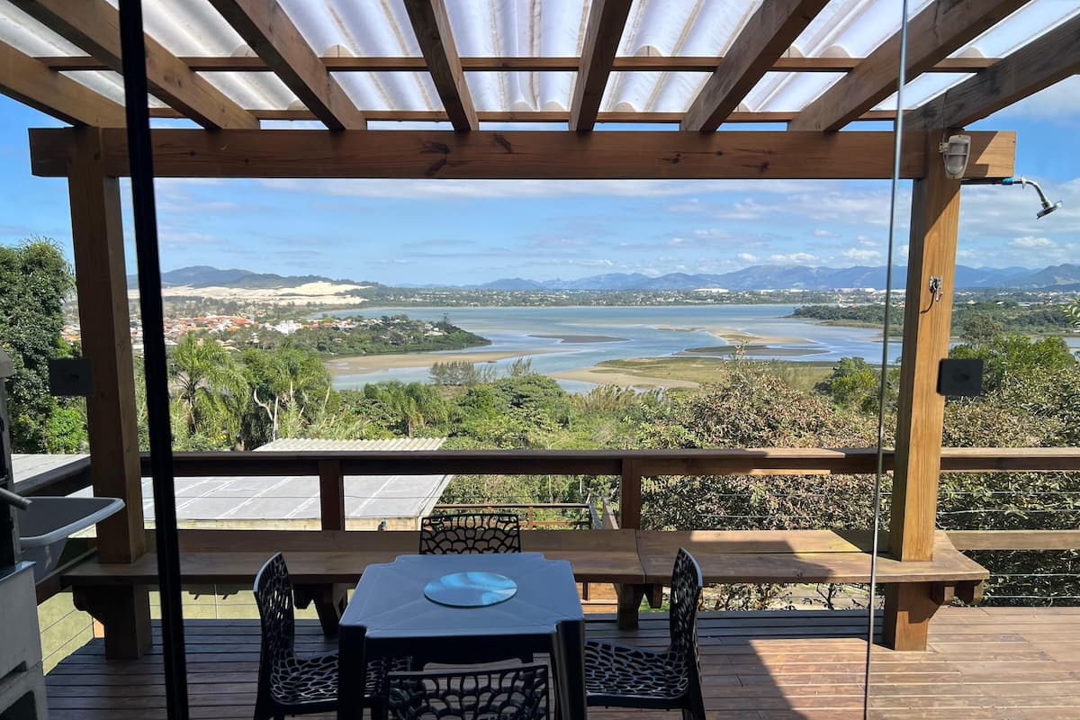 A wooden deck with a table and chairs, overlooking a scenic view of a river and distant mountains.