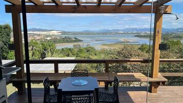 Um deck de madeira com mesa e cadeiras, com vista para um rio e montanhas ao longe.