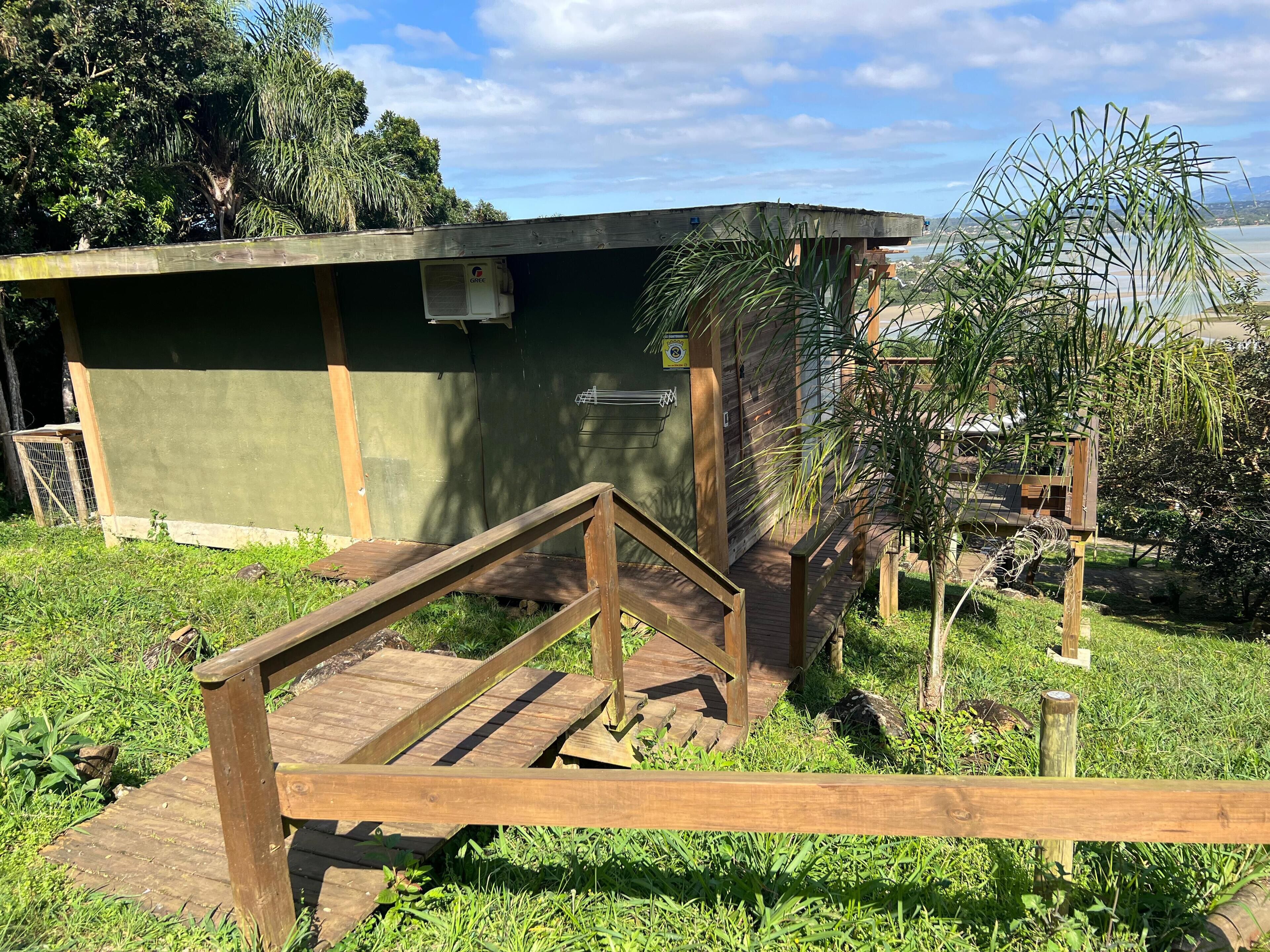 Um deck de madeira com uma rampa que leva a um edifício verde e uma pequena estrutura anexa.