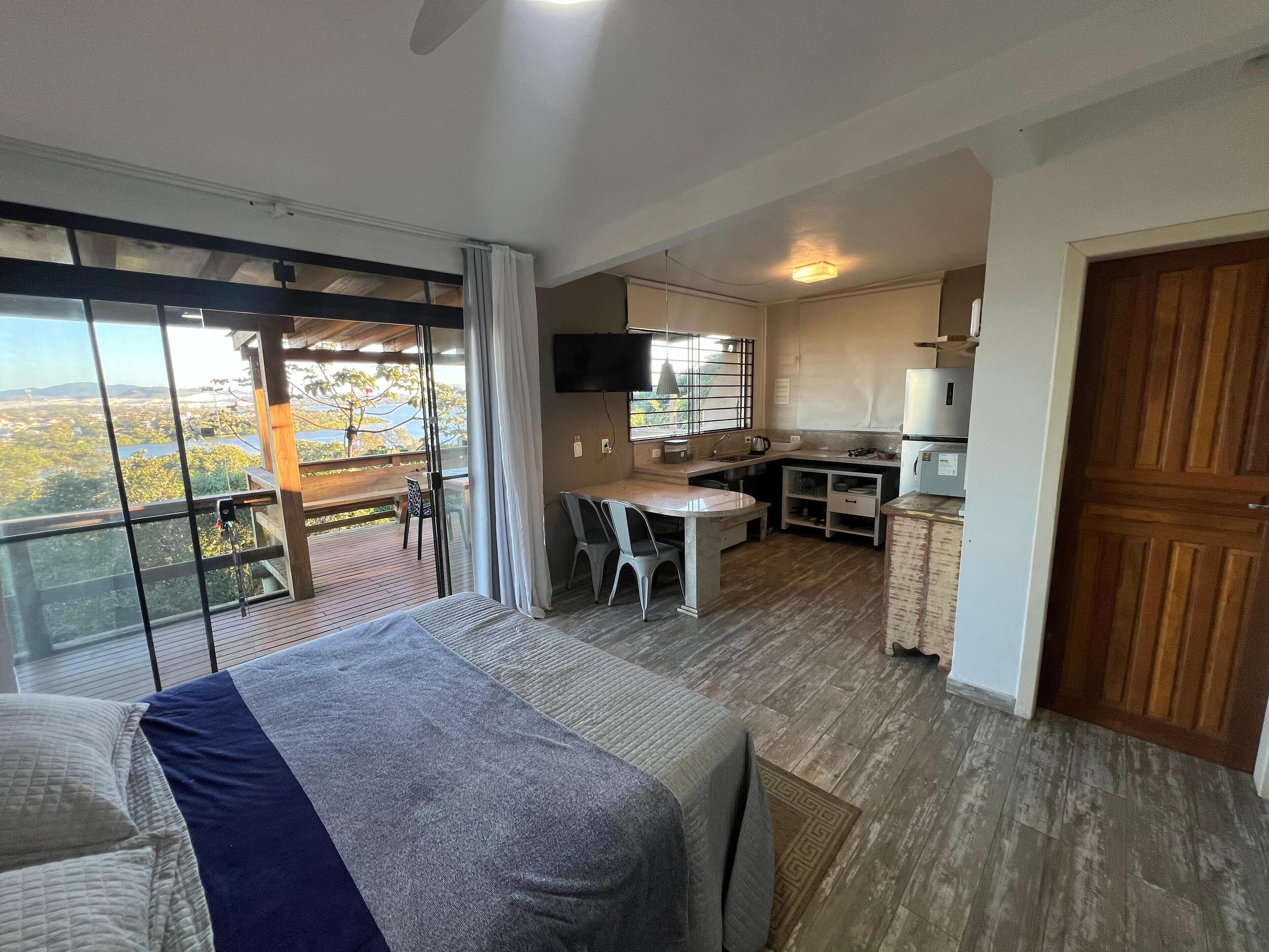Una habitación con cama, mesa de comedor, zona de cocina y un amplio ventanal con vistas.