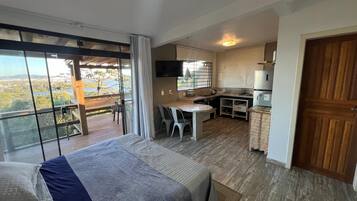 Una habitación con cama, mesa de comedor, zona de cocina y un amplio ventanal con vistas.