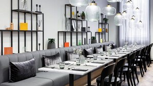 Un comedor moderno con una mesa larga dispuesta para varios comensales, rodeada de asientos tapizados en gris y sillas negras.
