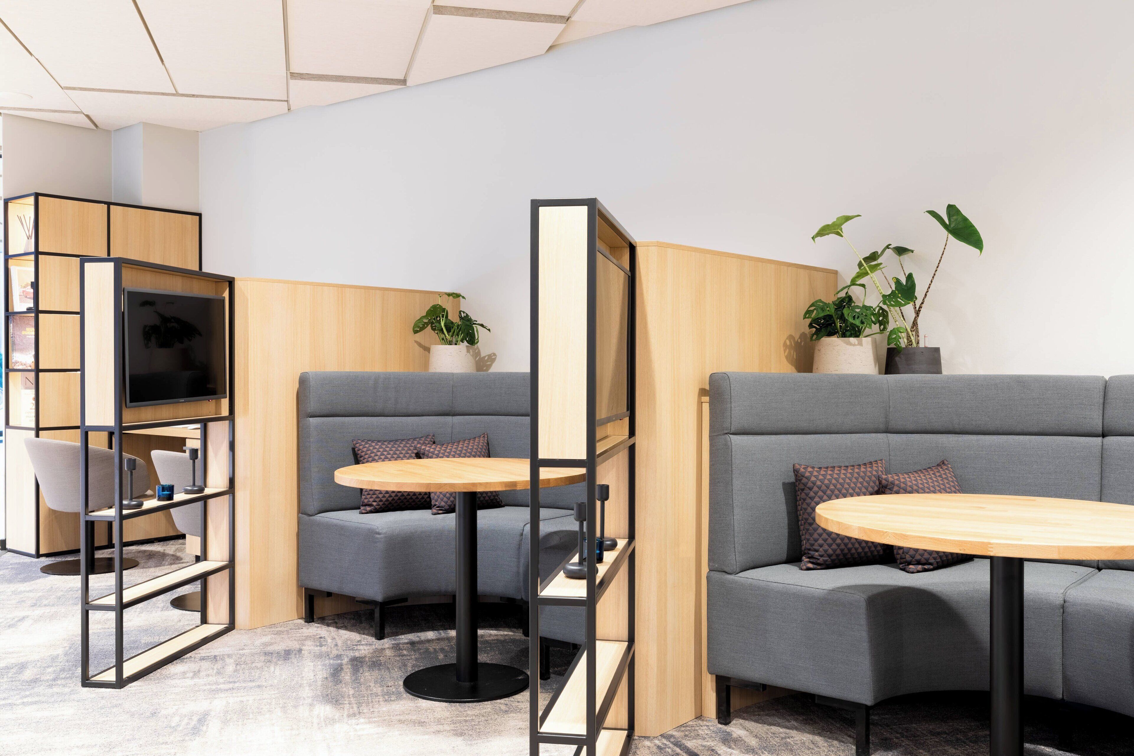 A modern lounge area with grey sofas, wooden tables, and a television.
