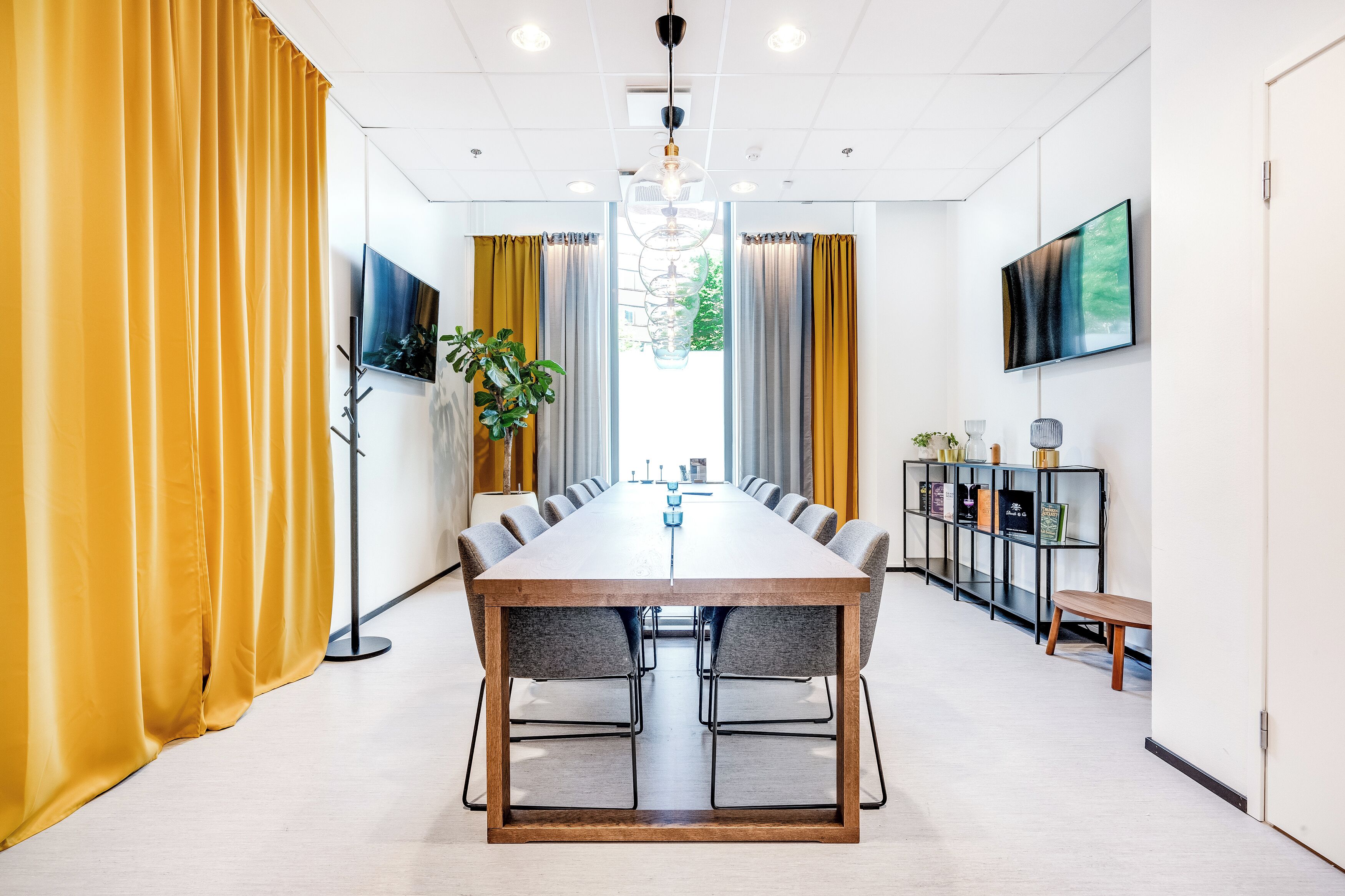 A conference room with a long table, chairs, a plant, a TV, and a bookshelf.