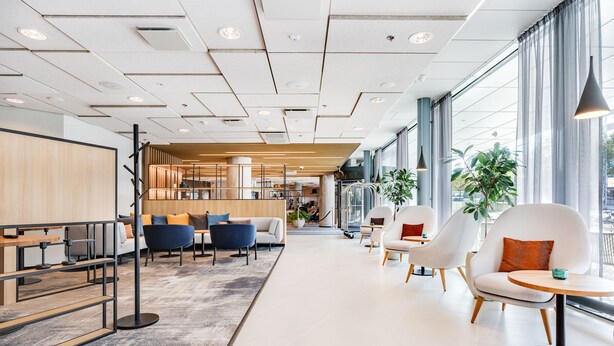 Un interior moderno con una zona de estar amplia, una escalera que sube a un nivel superior y ventanas grandes con vistas.