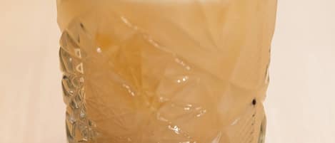 A clear glass with a textured pattern, a white foam layer, and a lemon peel garnish on a coaster.