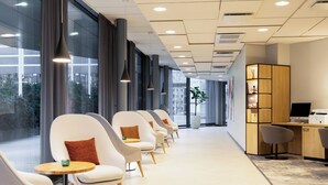 Ein moderner Wartebereich mit Reihen weißer Stühle, einem Holztisch mit Computer und einem großen Fenster mit Blick ins Freie.